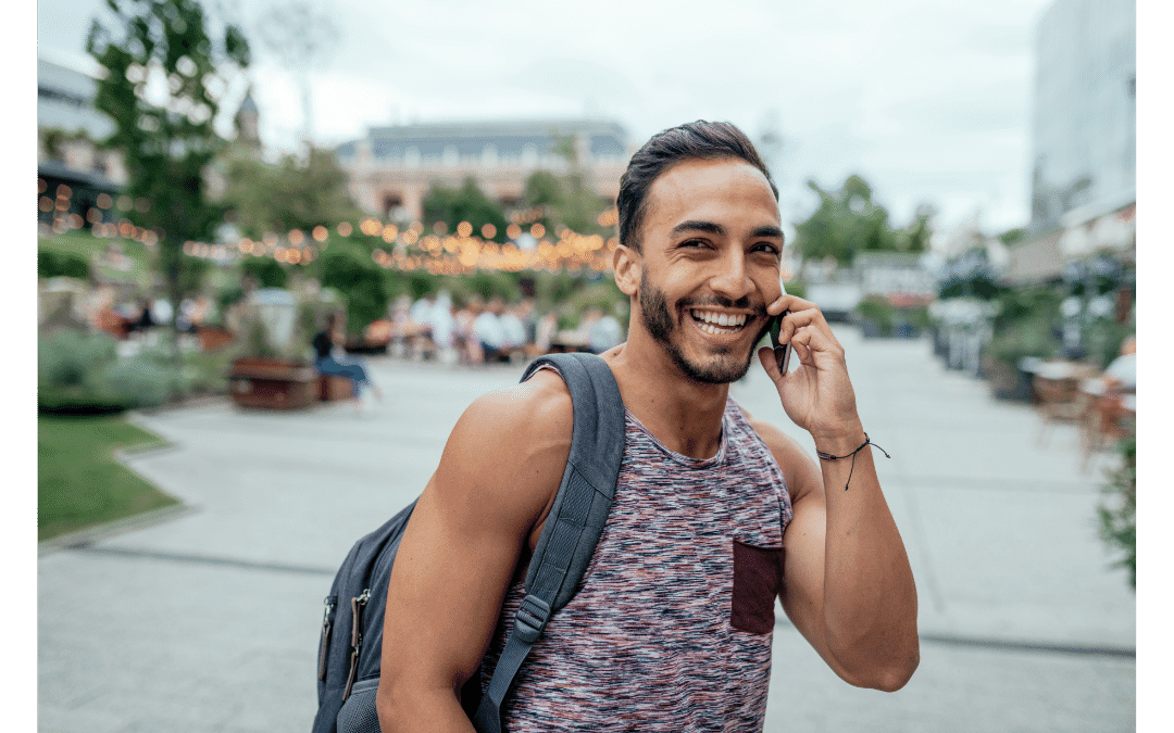 Man smiling, using phone outside with backpack on